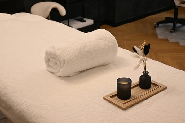 pexels photo 35884499 35884499 A serene spa massage table setup with a rolled towel, candle, and decorative vases in a relaxing environment.